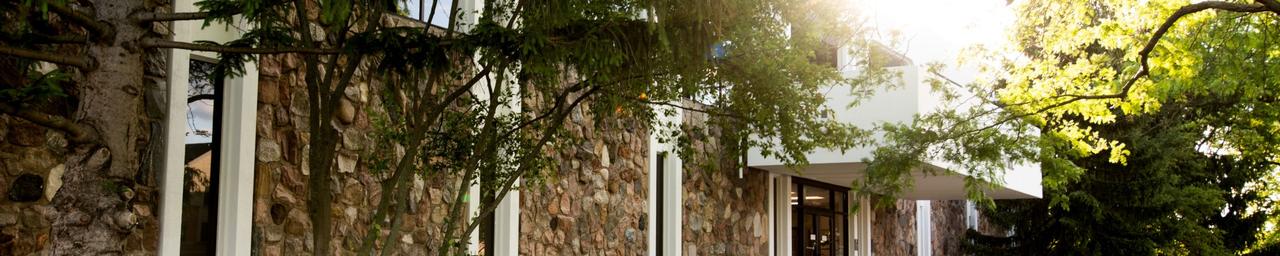 Lake Michigan Hall with green bushes and trees surrounding it with the sunrise peaking through